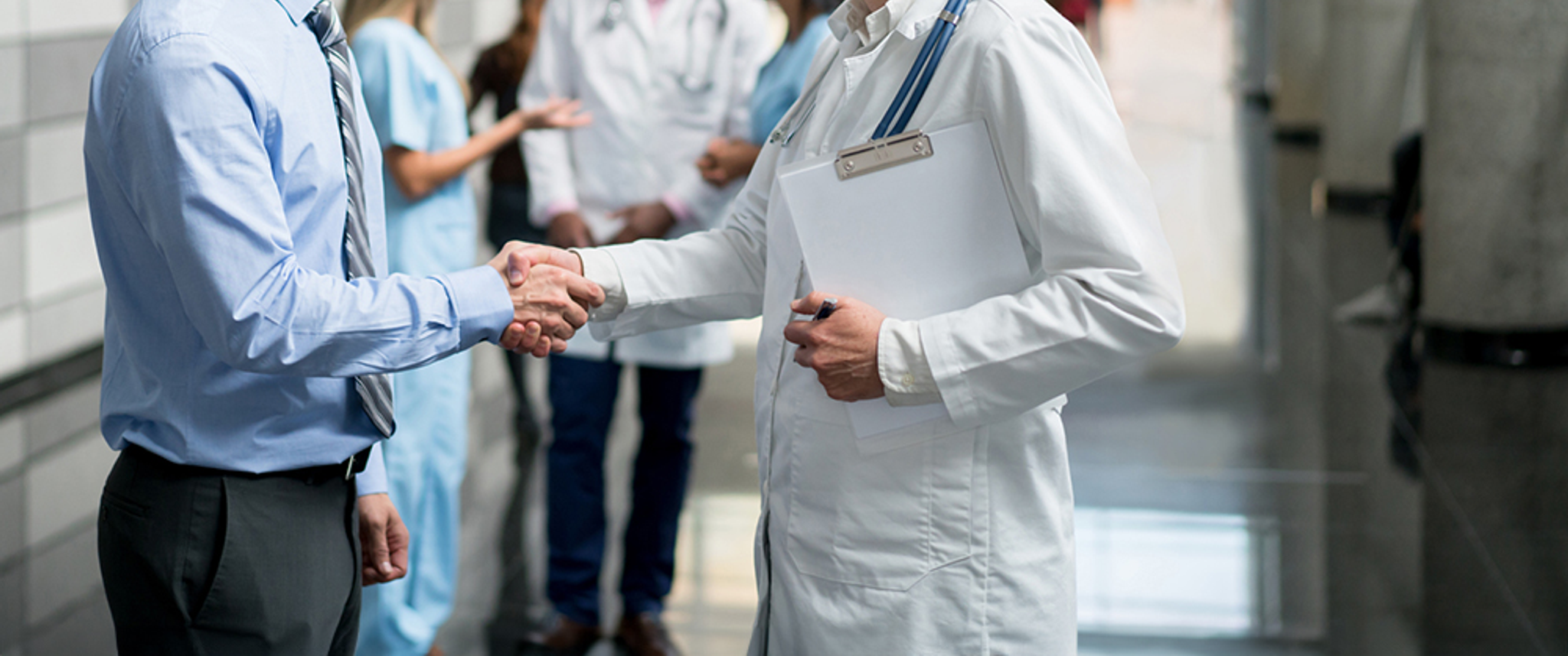 Two physicians shake hands in a hallway