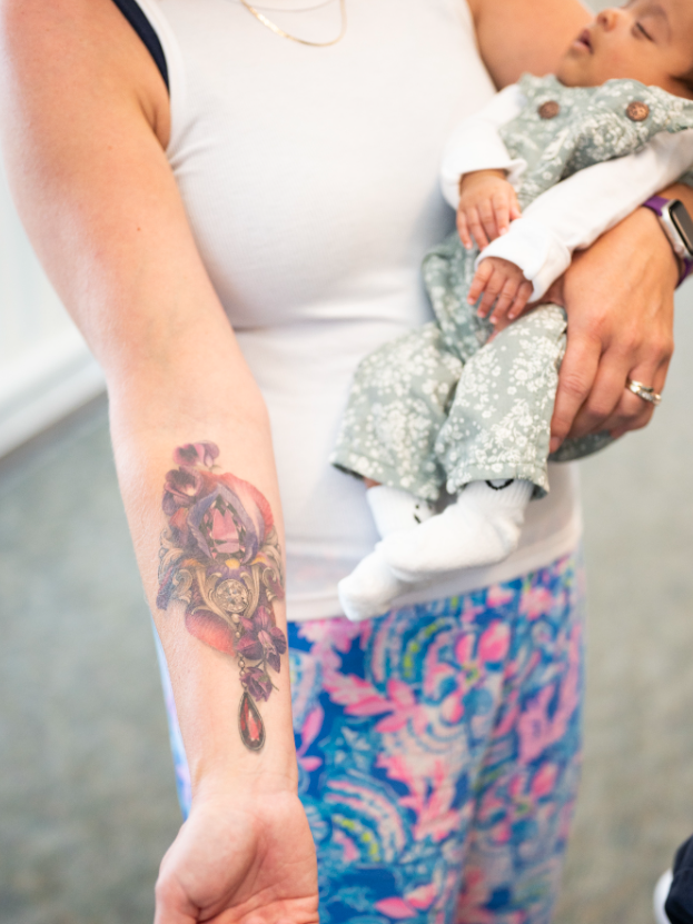 A tattoo on Sara Leister's arm showing a uterus adorned with birth stones and flowers