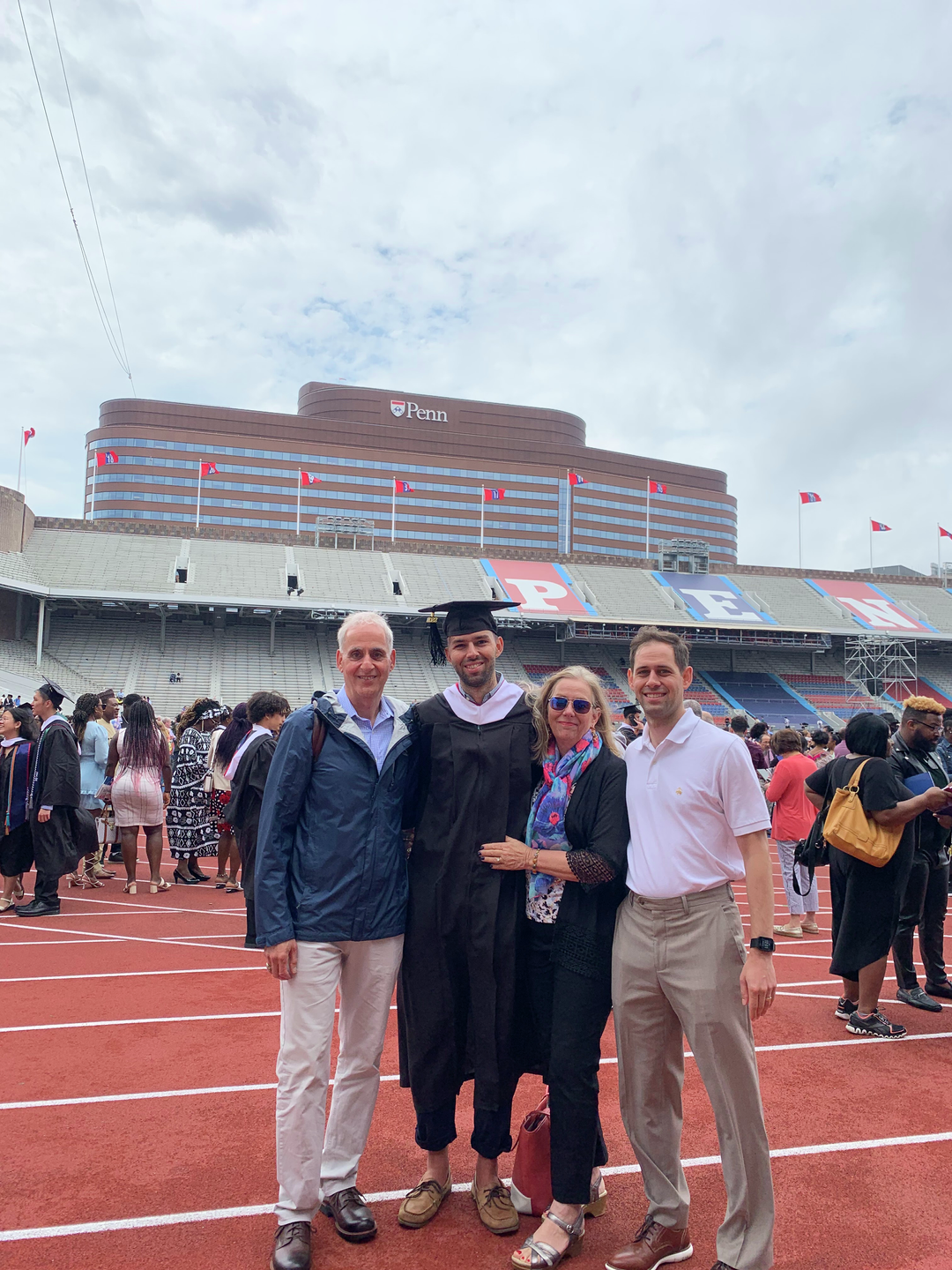 Chris Baccash, in a cap and gown, with his parents and brother after graduating from his Penn master’s program