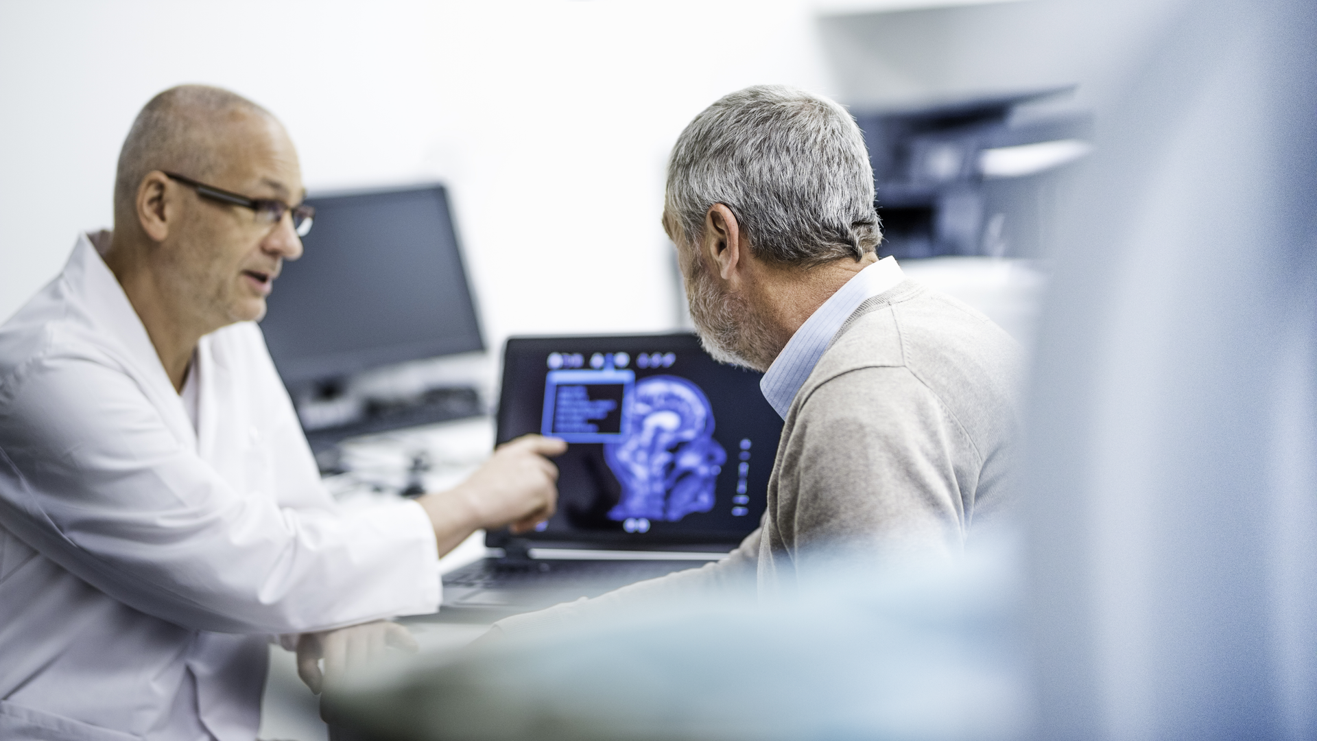 Male doctor in a lab coat talking to an older man about his brain scan.