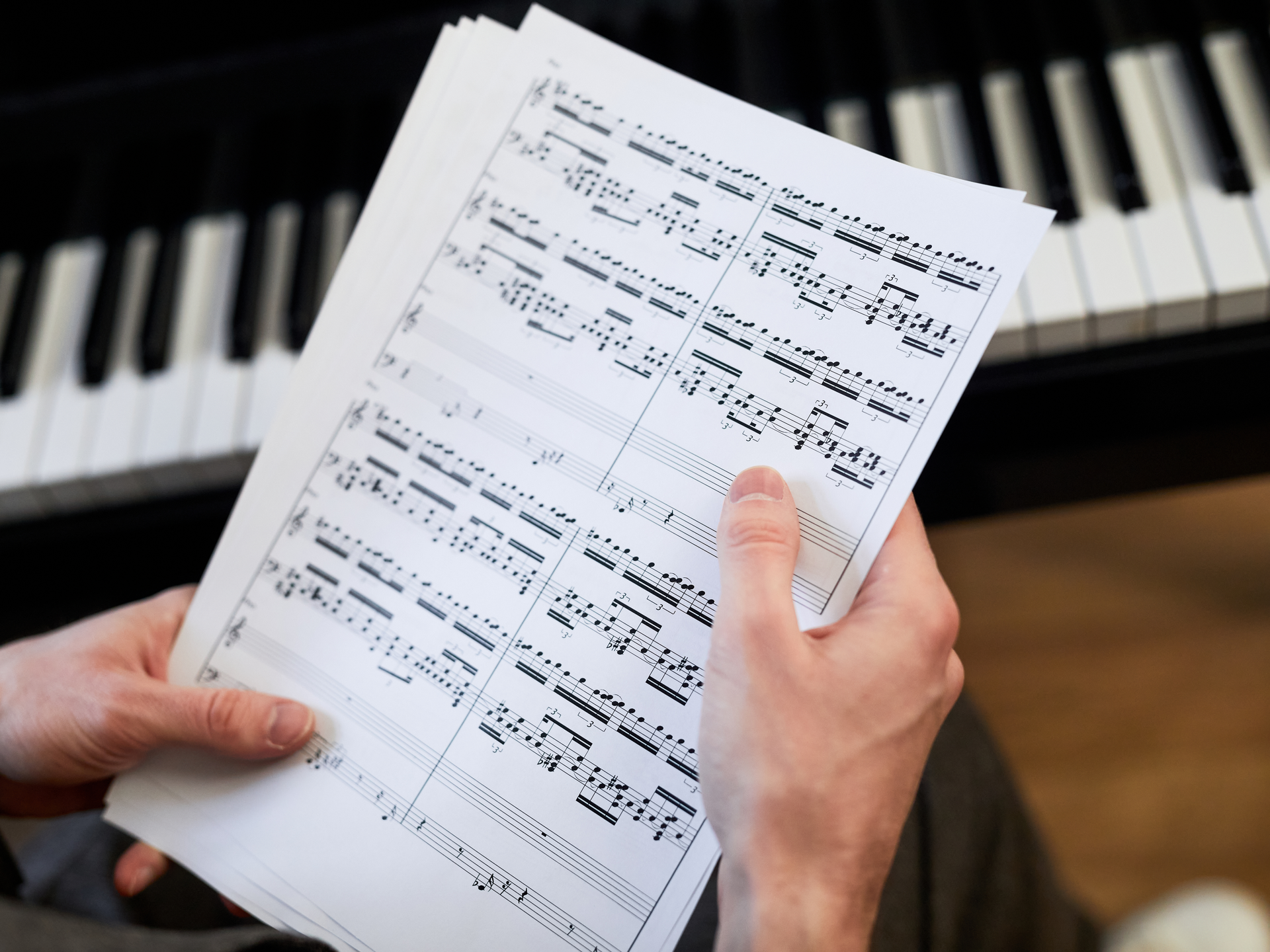 Close-up of hands holding sheet music above a piano