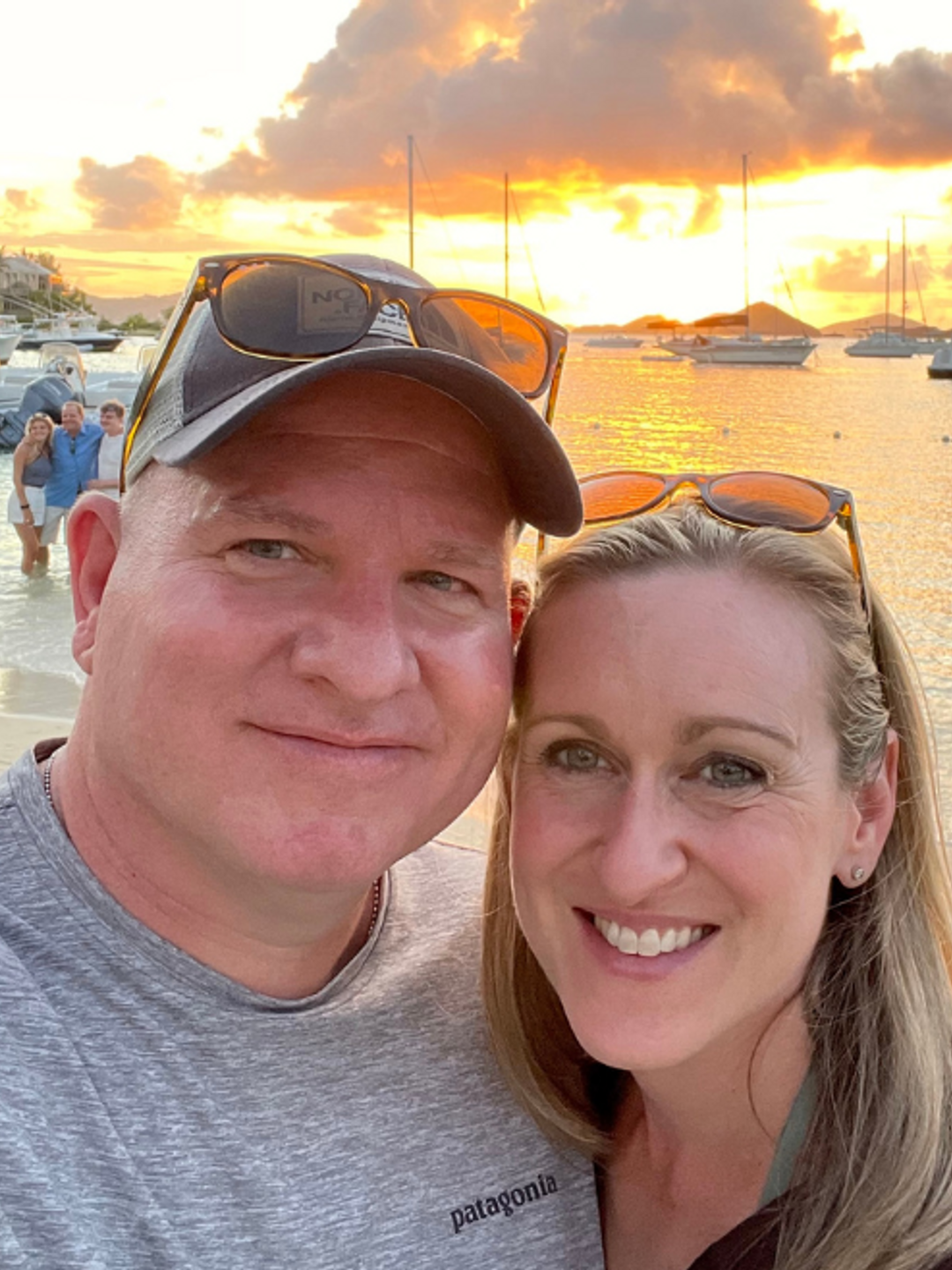 Kim Bello and her partner standing on beach with water and boats in background