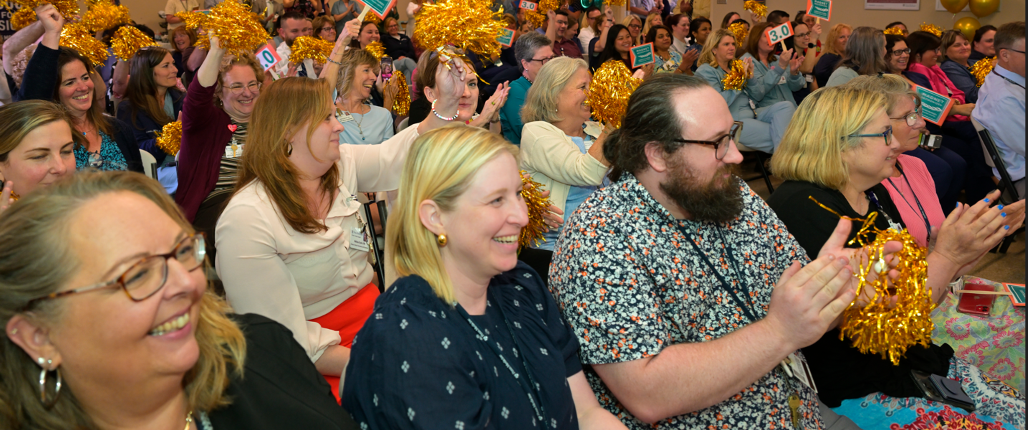 A group of nurses and staff seated in an auditorium cheer and smile