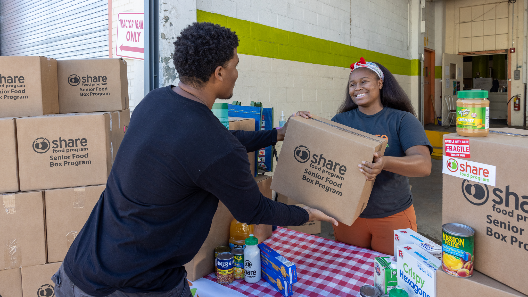 A man reaches across a table to accept a box labeled "Share Food" from a smiling woman