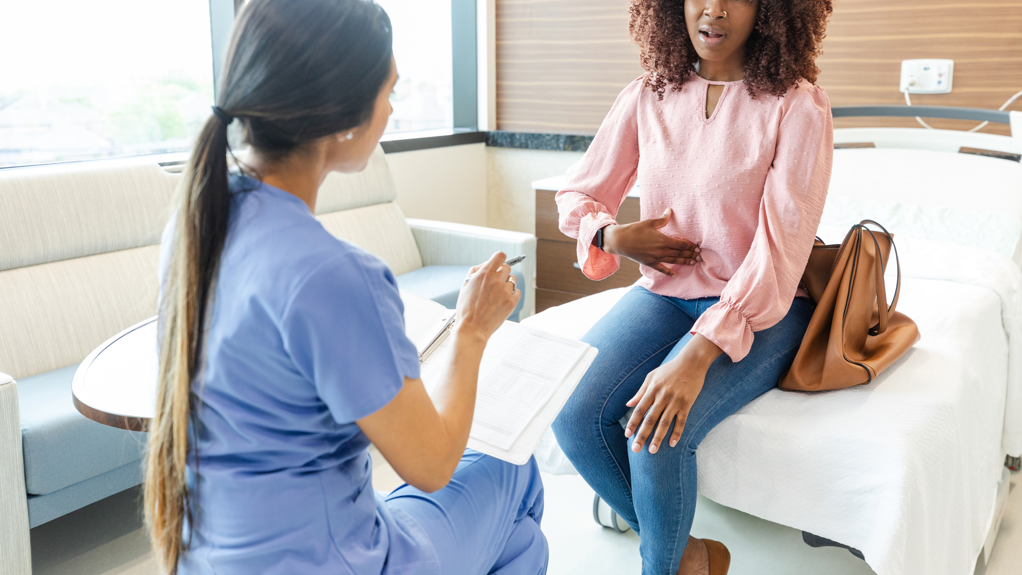 Adult woman gestures toward her abdomen as she describes her abdominal pain to an female healthcare professional