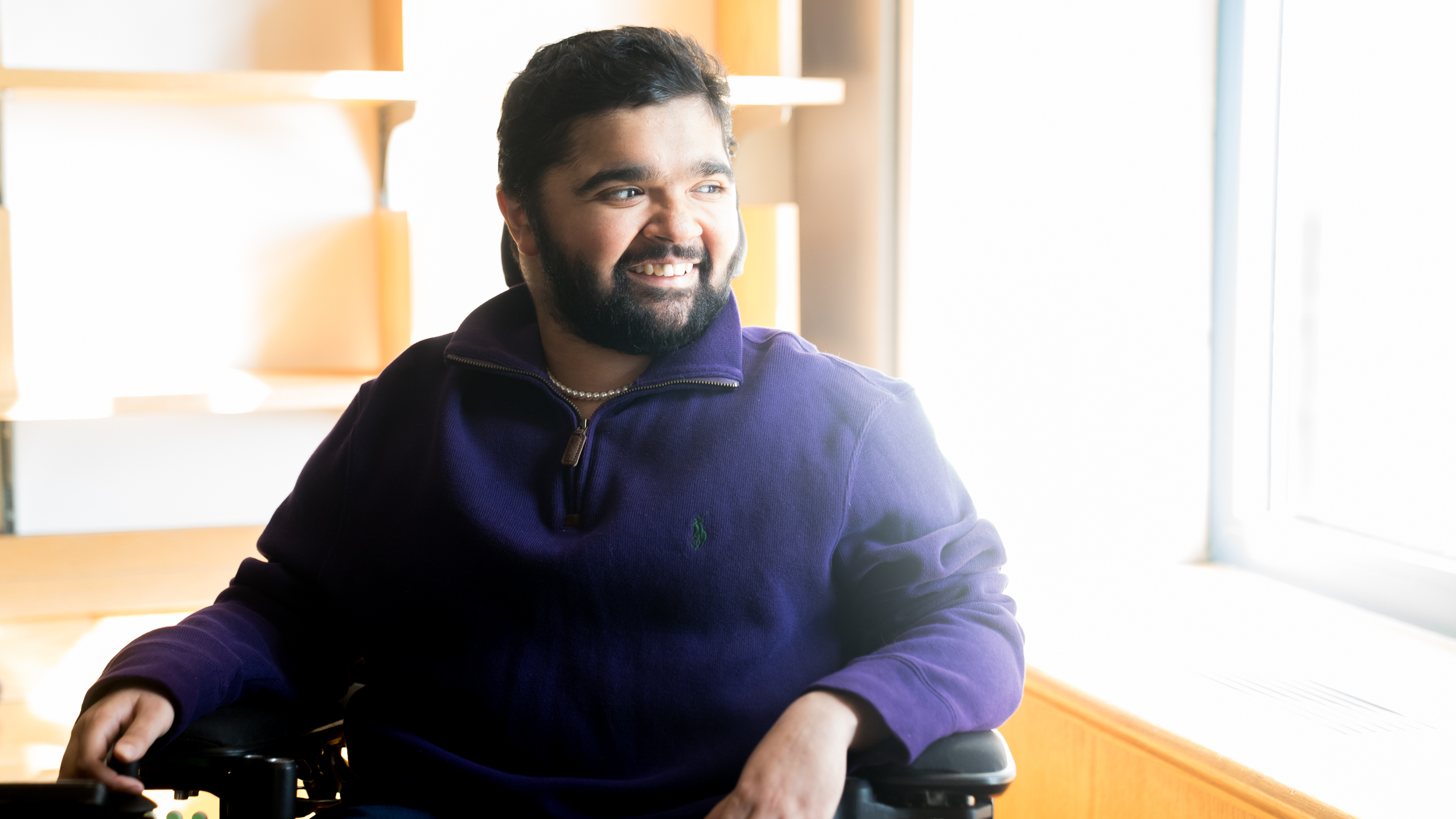 Yuva Gambhir, a young man with a beard sitting in a motorized wheelchair, looks out a sunny window