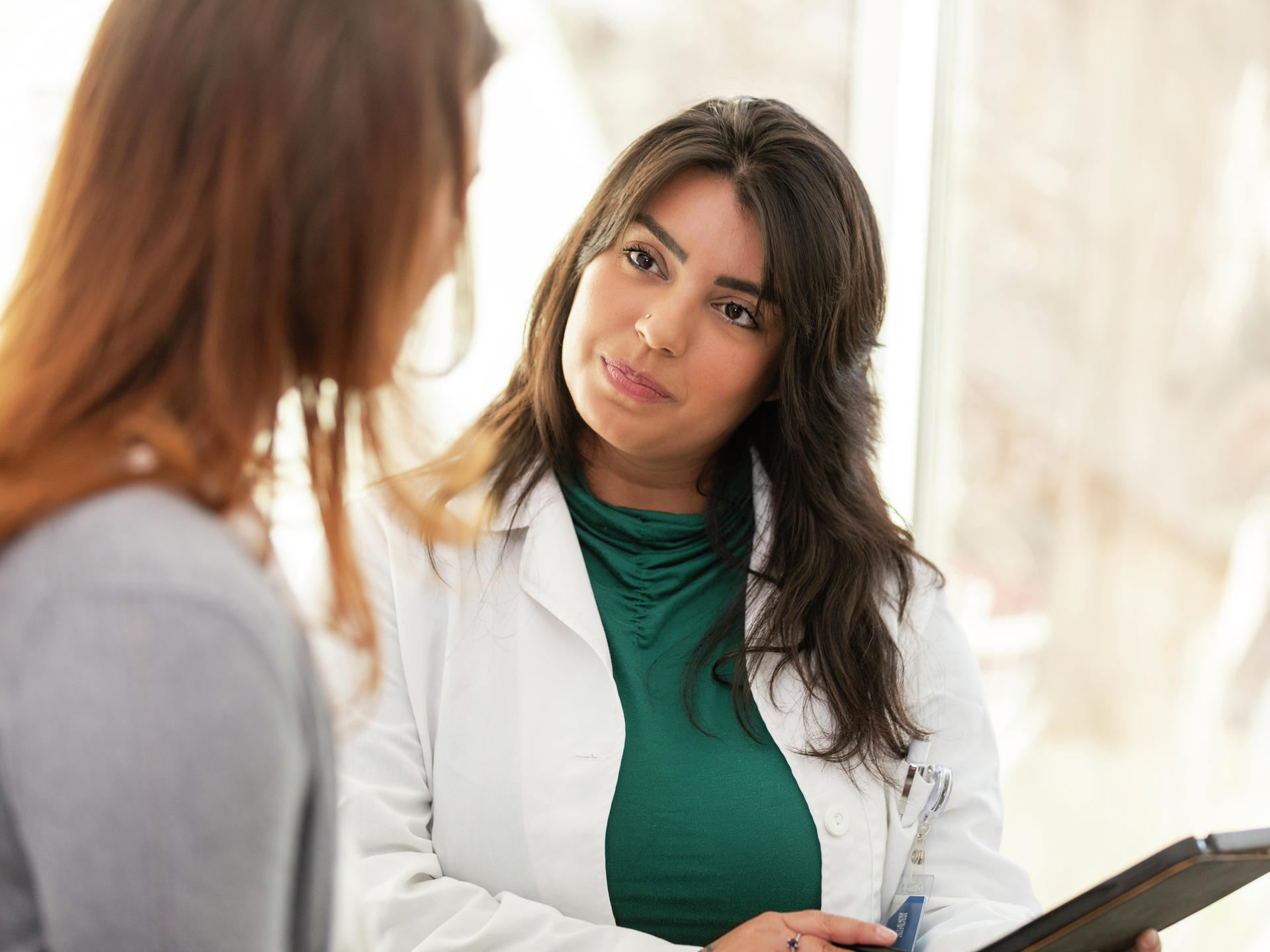 Female doctor holds a digital tablet while listening attentively to the unrecognizable female patient