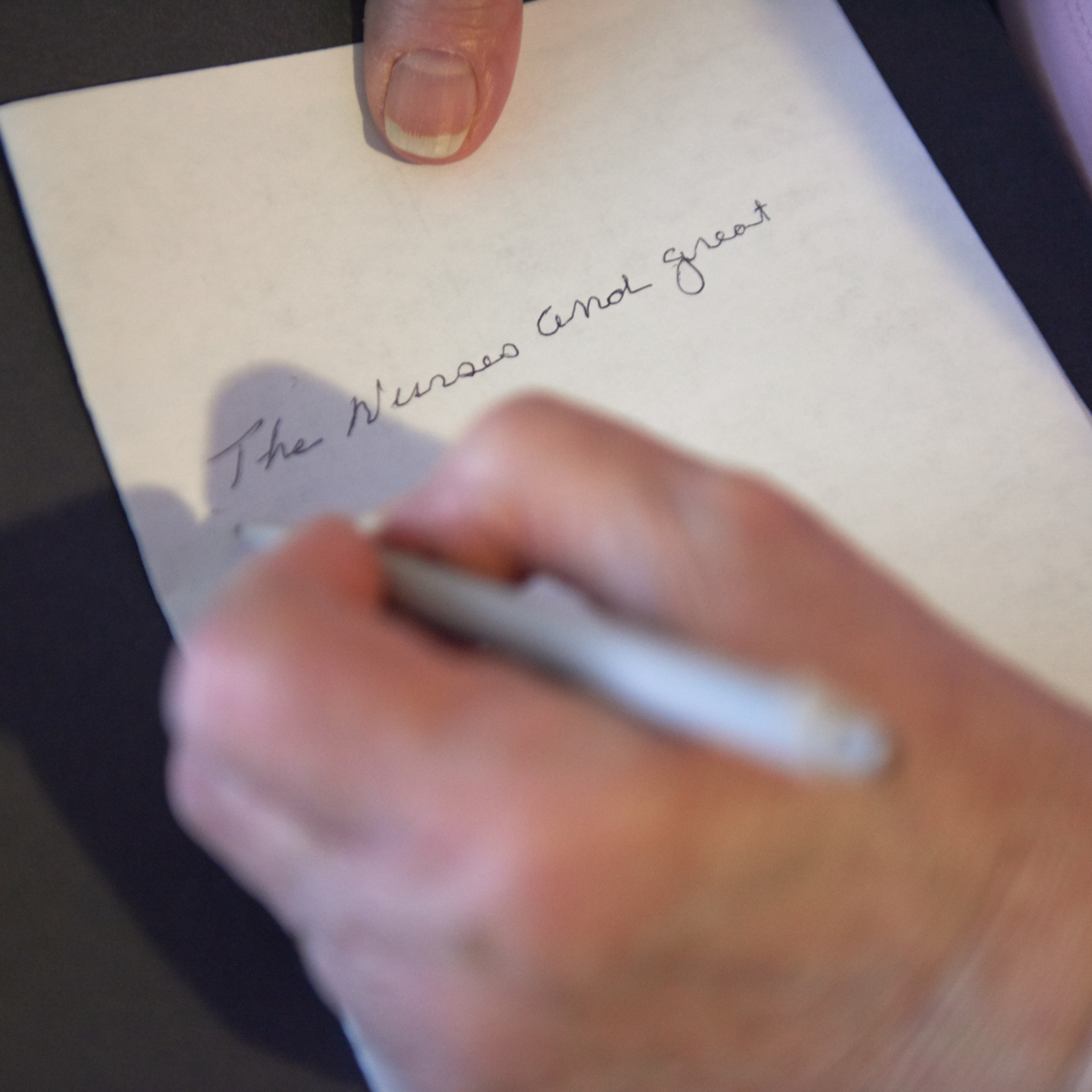 An older person's hand is writing the phrase "the nurses are great"