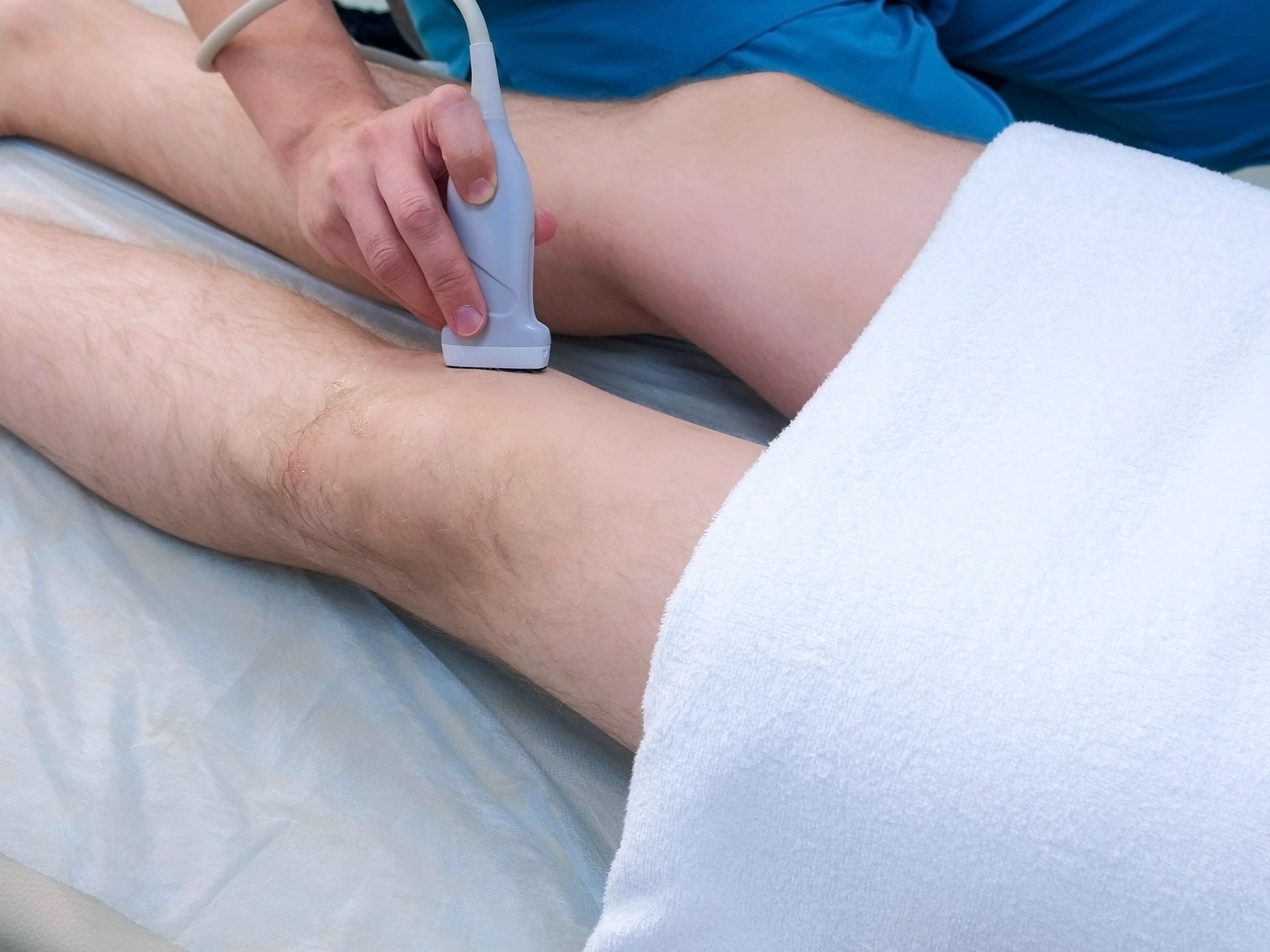 Healthcare provider using an ultrasound scanner on a male patient's leg during a diagnostic examination.