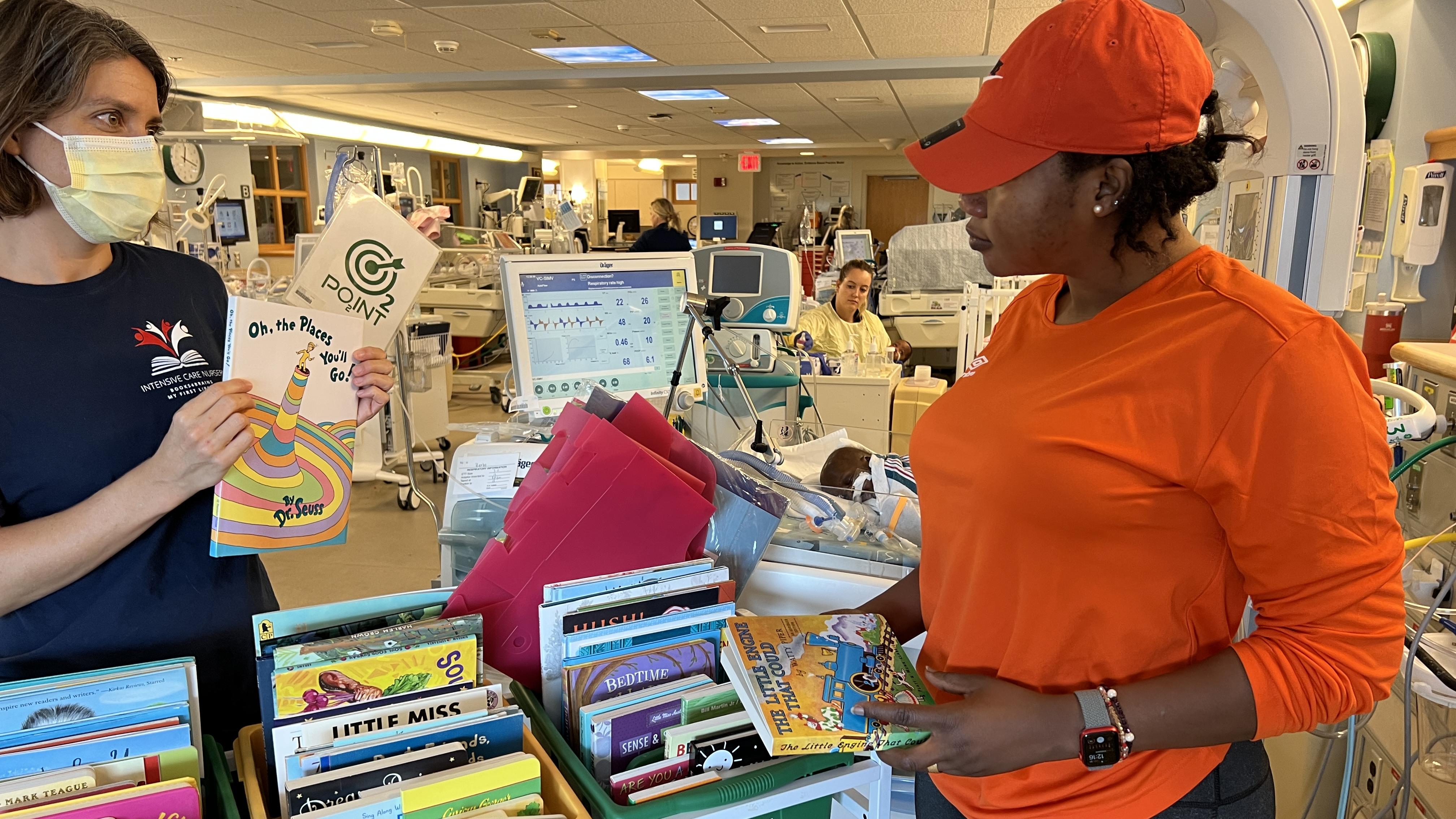 Boura Zerbo holds several children's books while Whitney Zachritz holds up a selection of more books from the cart between them.