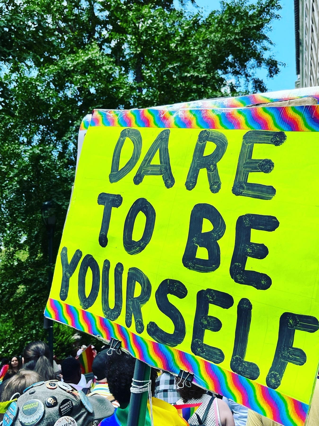 A hand-painted sign on a bright yellow background says "Dare to Be Yourself."