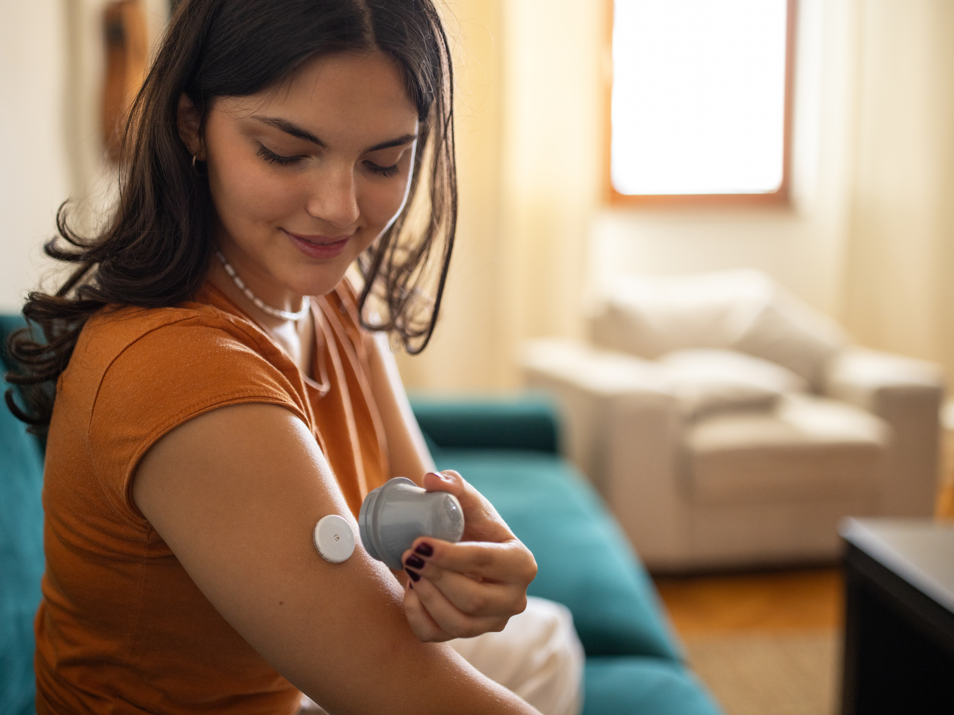 A young woman smiling and  looking down at her arm where she has just administered a Continuous Glucose Monitor.