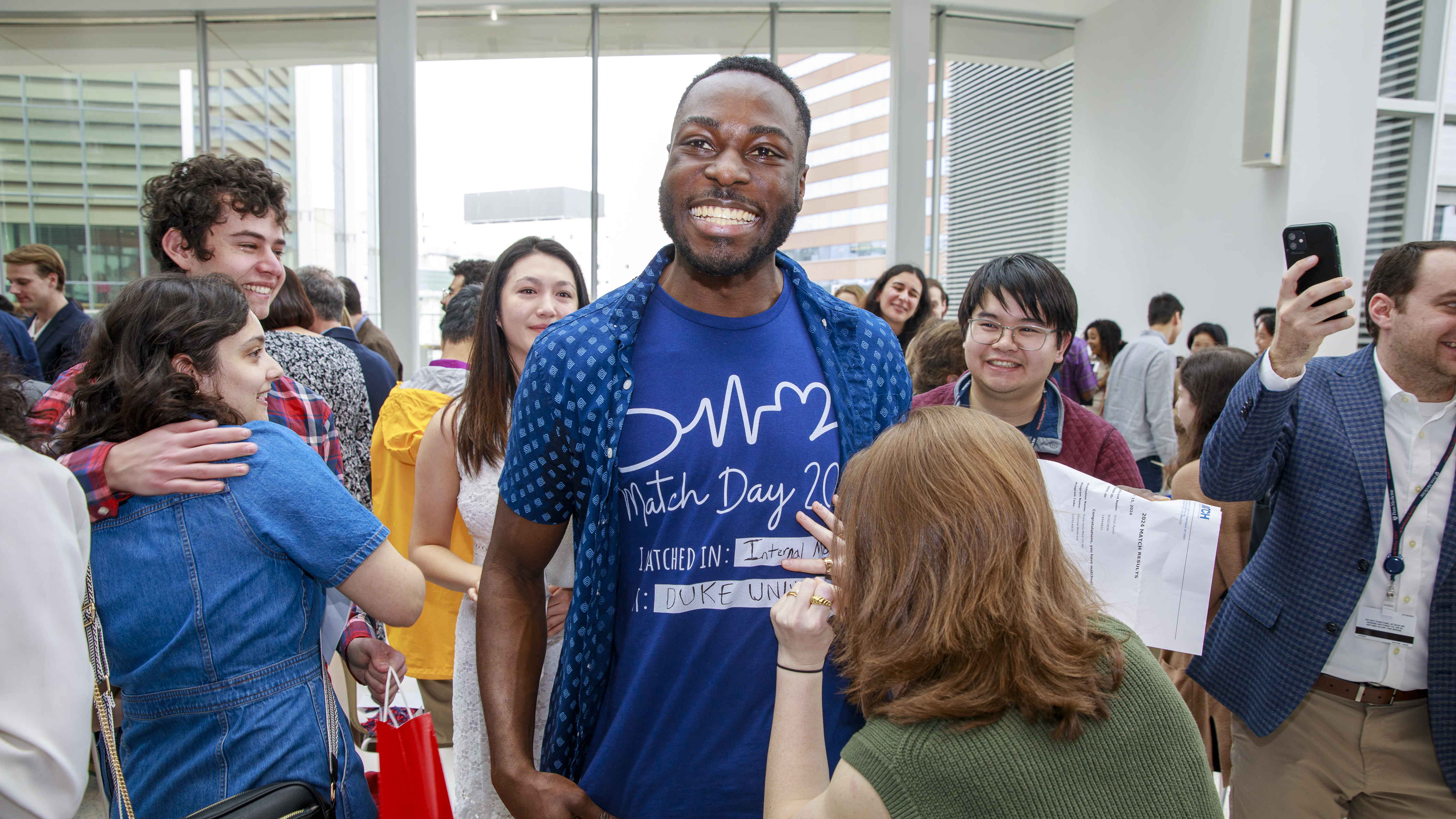 Victor Ayeni standing and smiling as his residency match, Duke University, is written in marker on his t-shirt