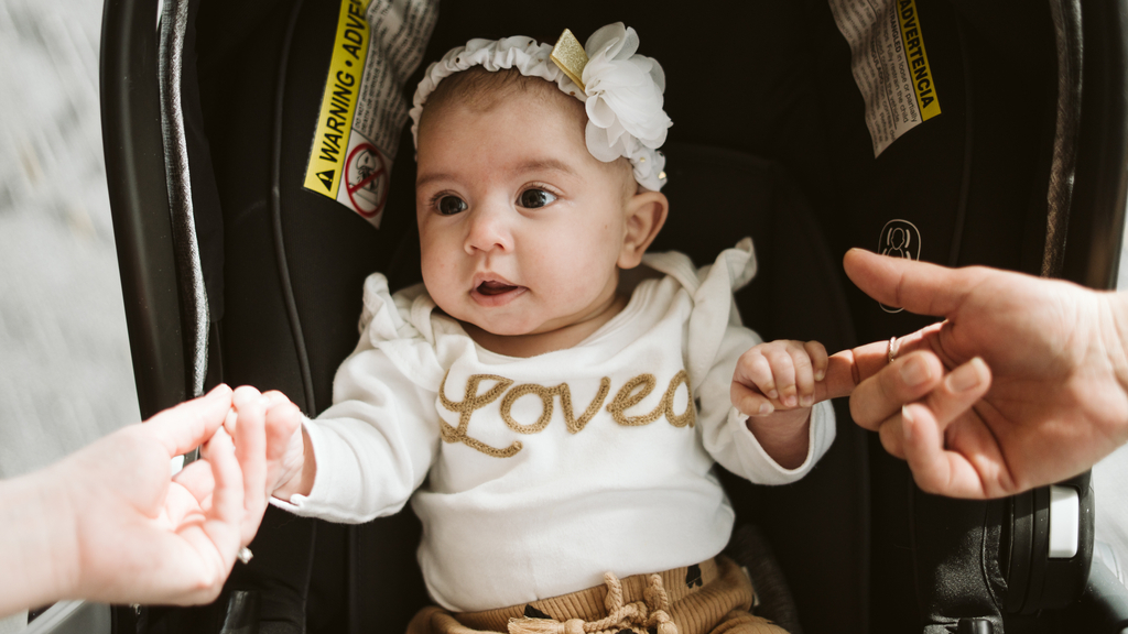 Baby Adrianna, wearing a shirt that says "Loved," holds in each hand a finger of her mother and her mother's uterus donor