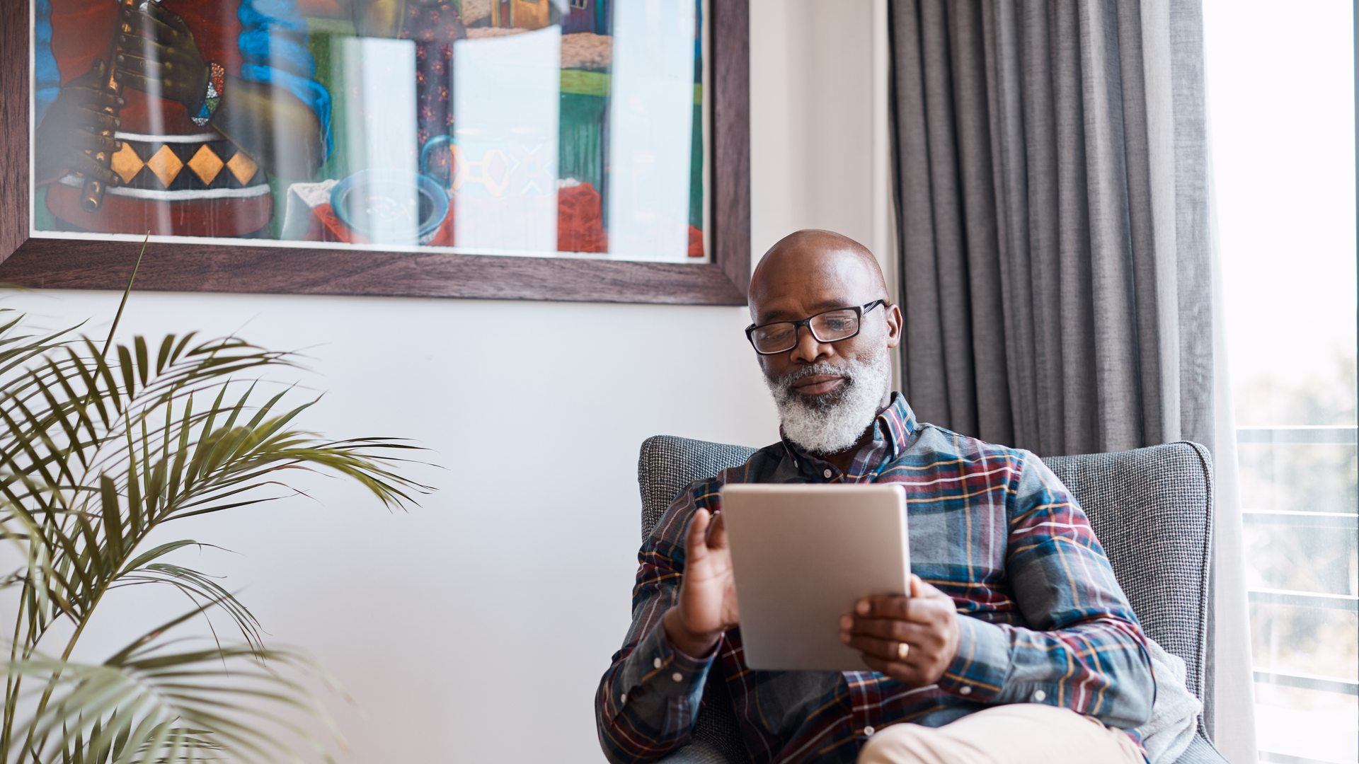 An older man sitting in his living room watching a video on his tablet.