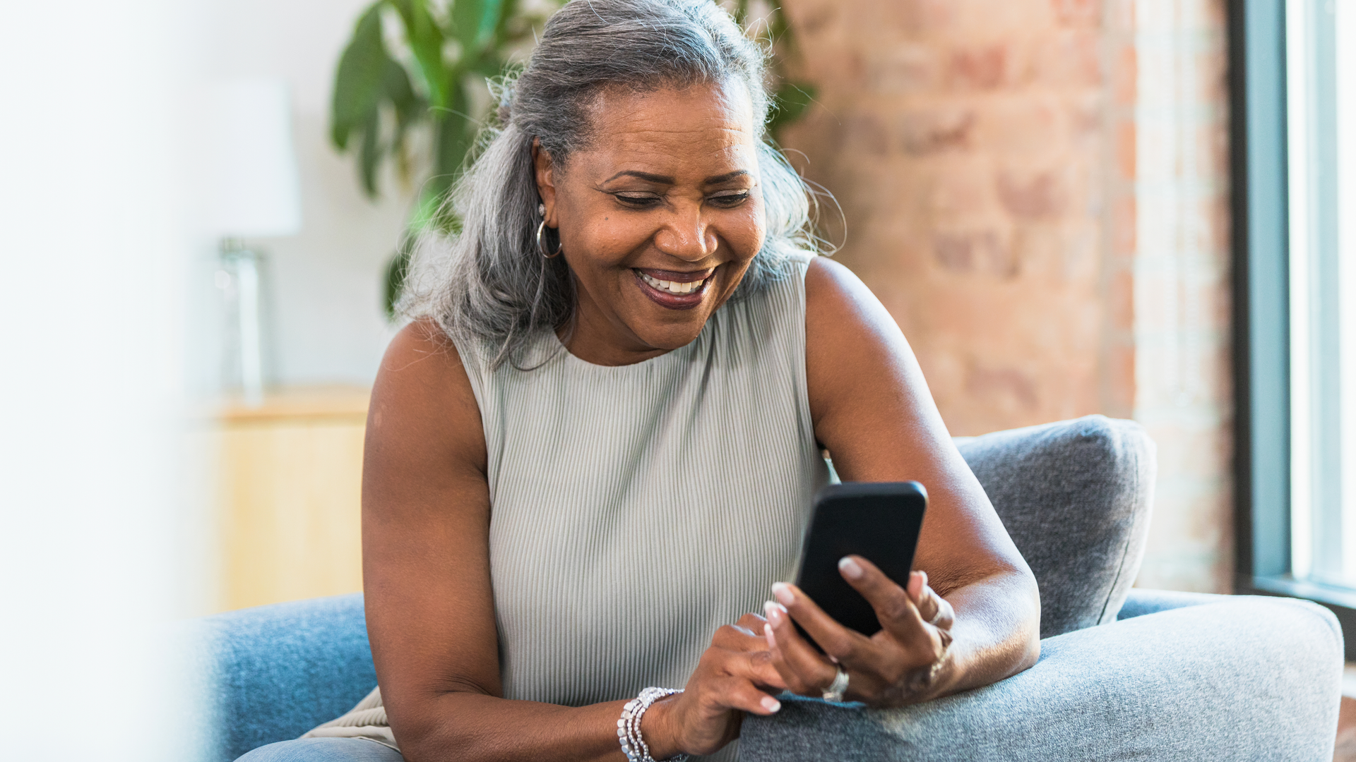 Smiling senior woman looking at her smart phone while sitting on a couch indoors