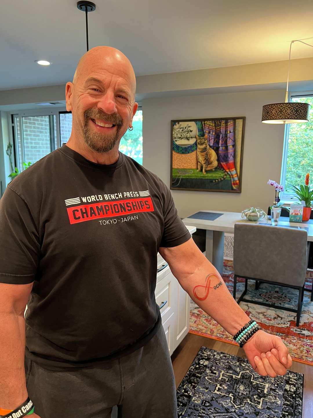 Howard Aaron, wearing a World Bench Press Championships t-shirt, shows a tattoo of a red infinity sign with the word Ocho next to it on his arm.