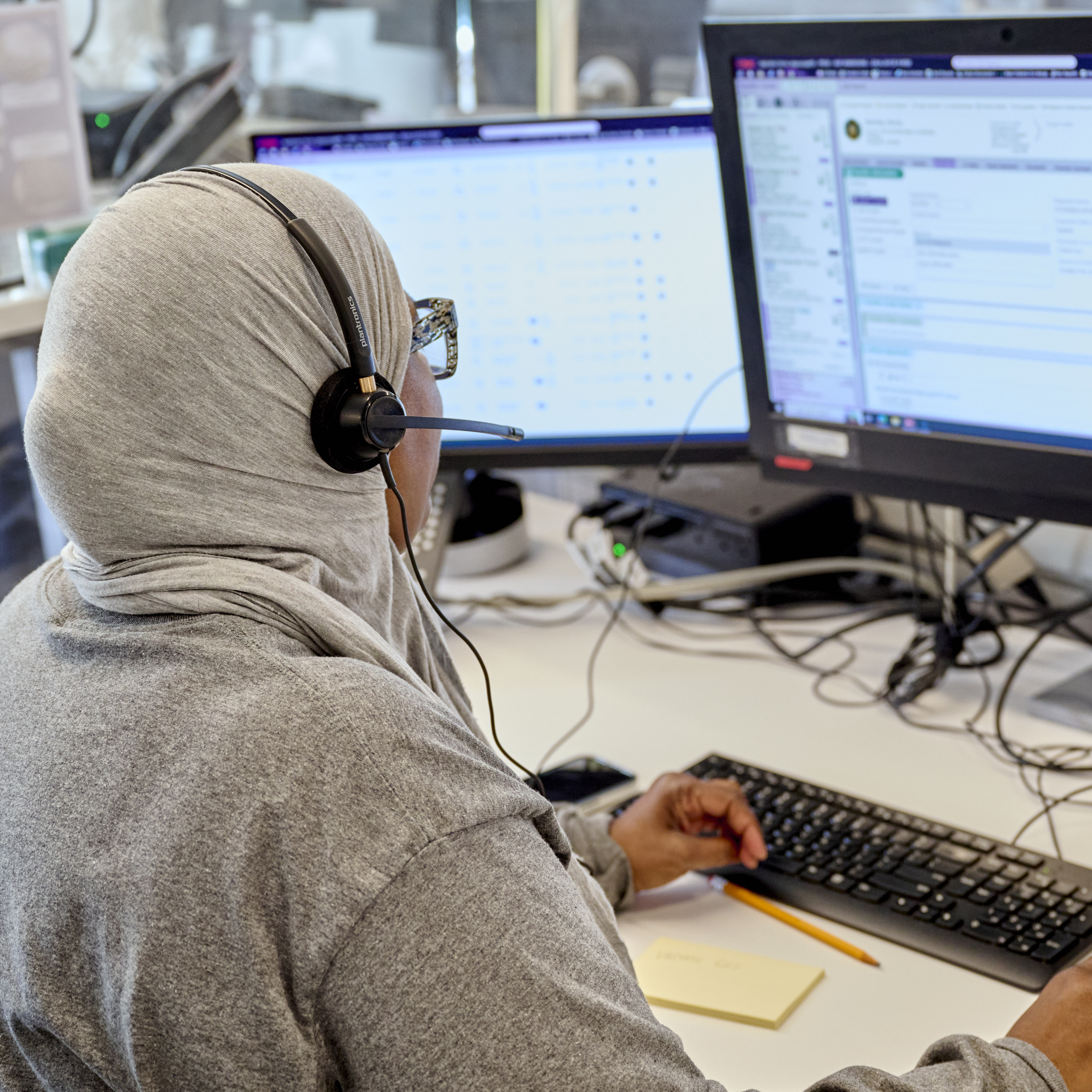 A woman wearing a headscarf and headset looks at a computer screen 