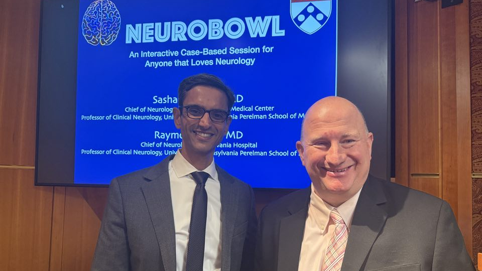 Sashank Prasad and Raymond Price in front of a screen showing the title Neurobowl with Penn logo and brain image