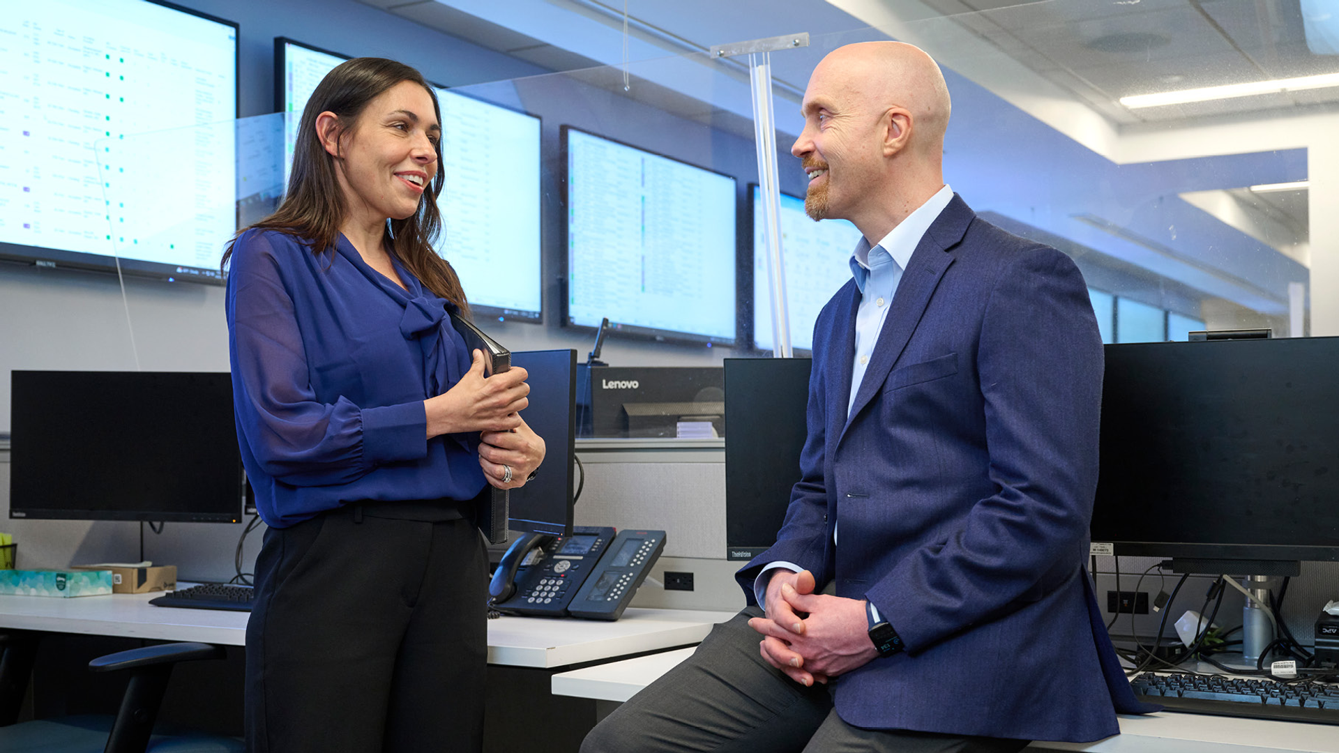Robin Wood and William Schweickert converse while sitting in an office filled with cubicles