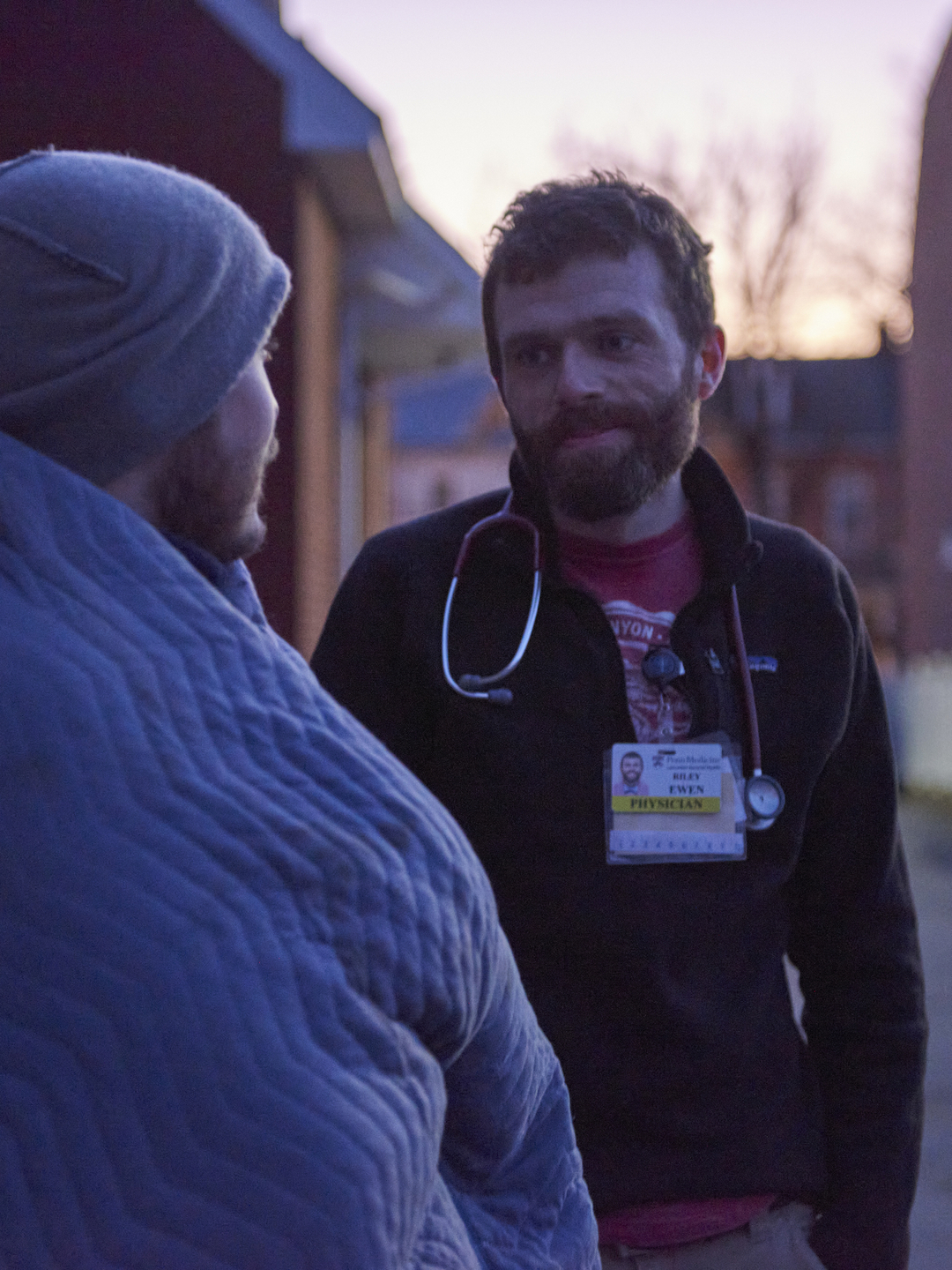 Dr. Riley Ewen speaks with a man wrapped in a blanket at twilight