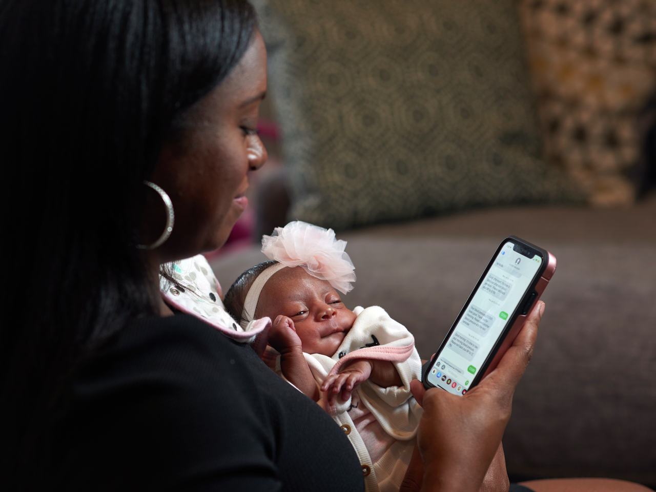 Karimah Ferguson, a young Black mother, holds her adorable baby while looking at text messages about blood pressure readings on her phone