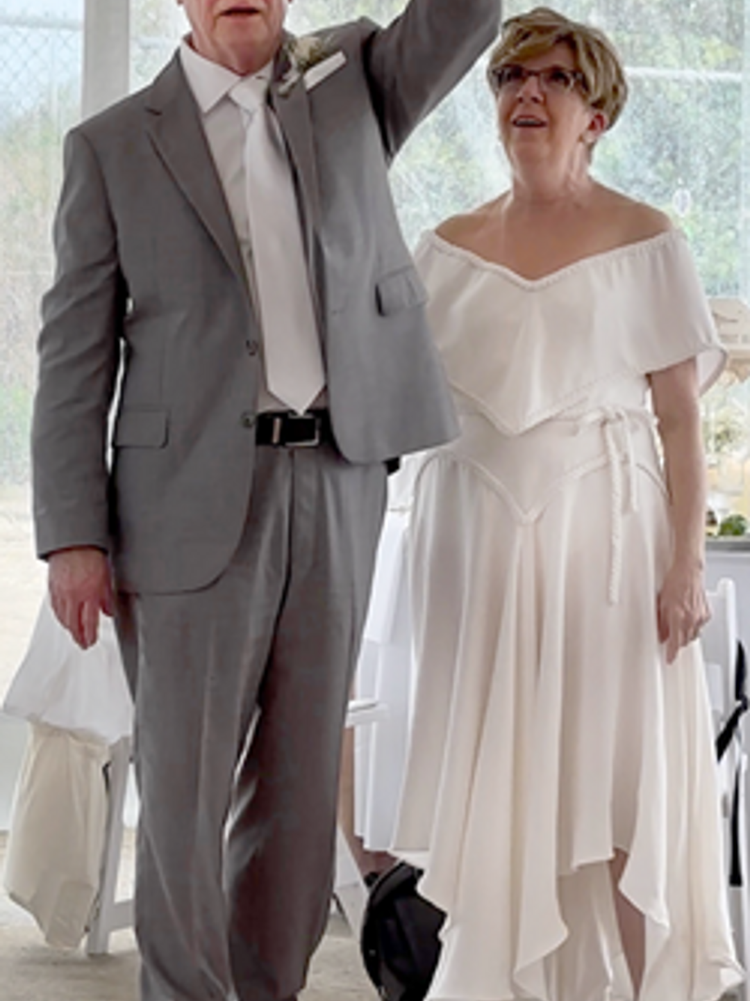 Jim McDevitt in a gray suit making a toast next to an older woman in a white dress.