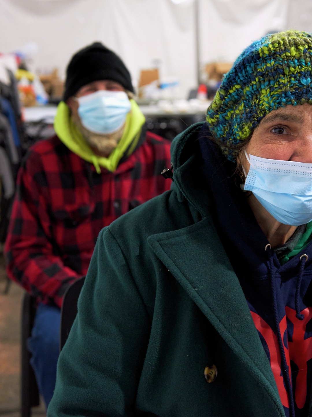 Rose, a 54-year-old woman wearing a knit cap, winter jacket, and face mask, looks at the camera with a soulful expression
