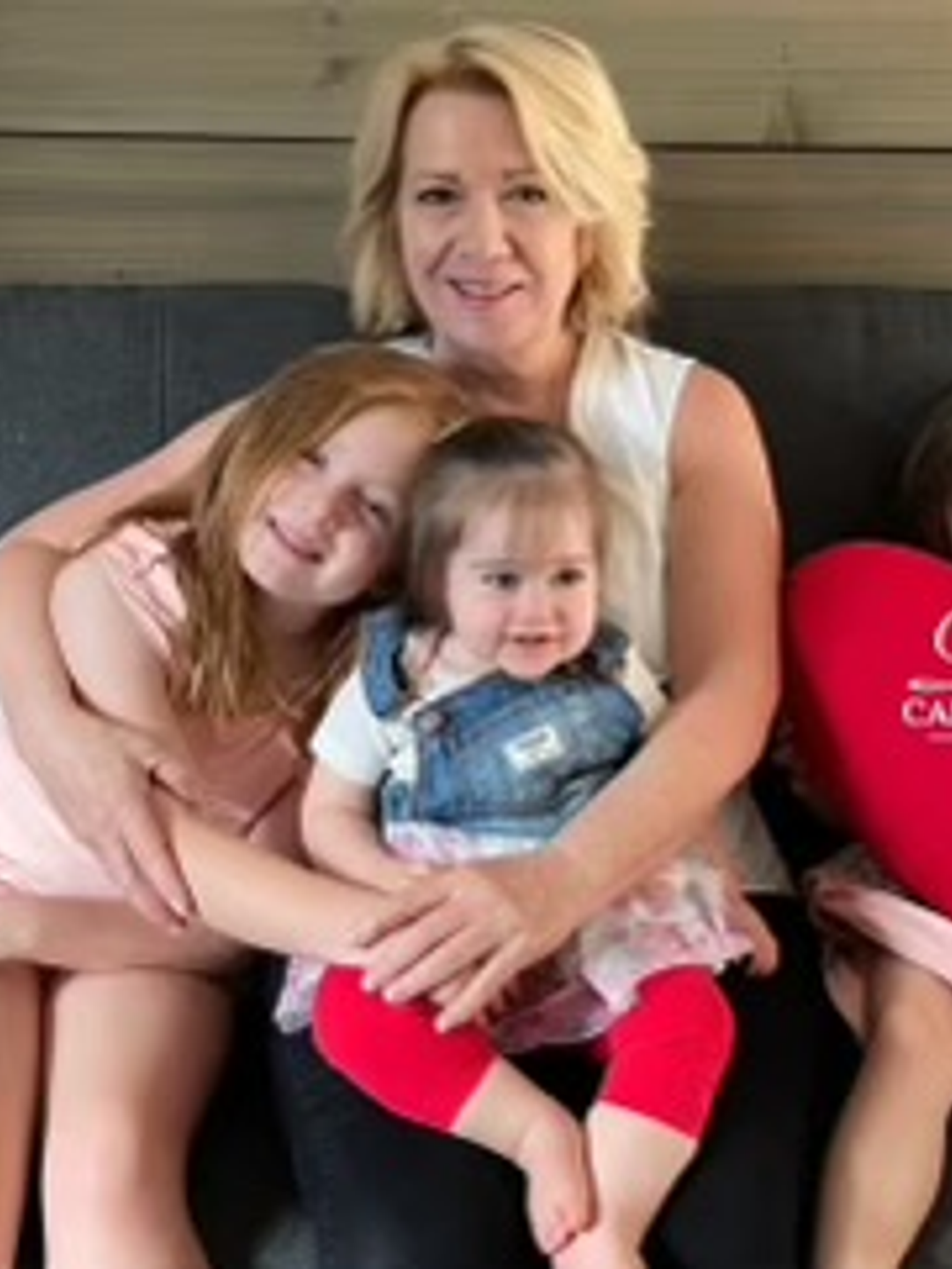 Susan Helfrich hugging her three young grandchildren, holding a Penn Cardiac Care heart pillow