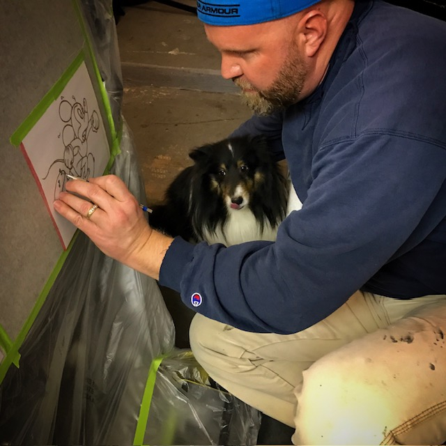 Mike squatting down, sketching Mickey Mouse, with dog next to him