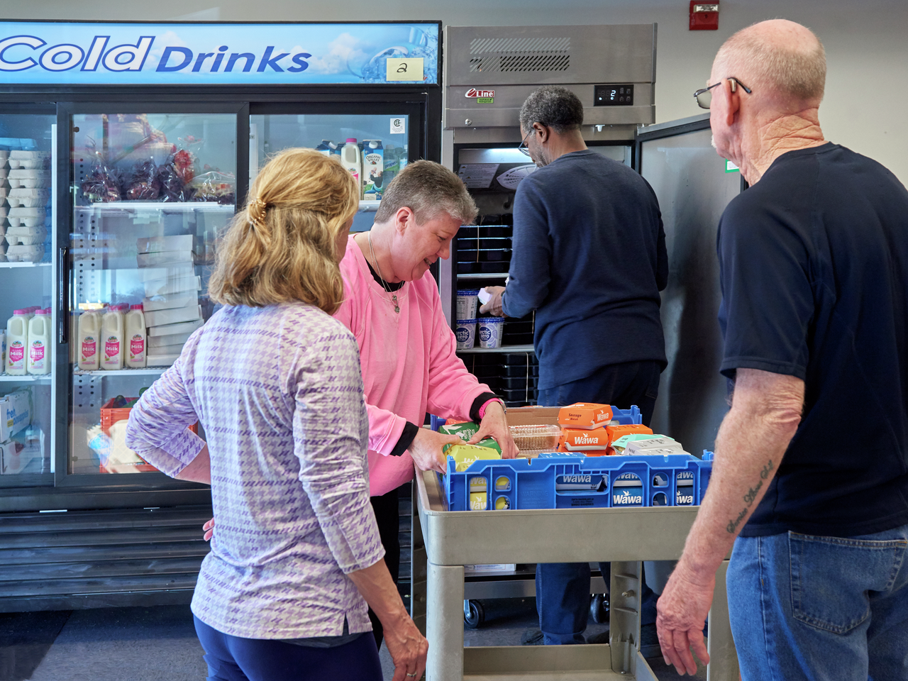 Several people unpack Wawa food from a crate and load food into commercial refrigerators