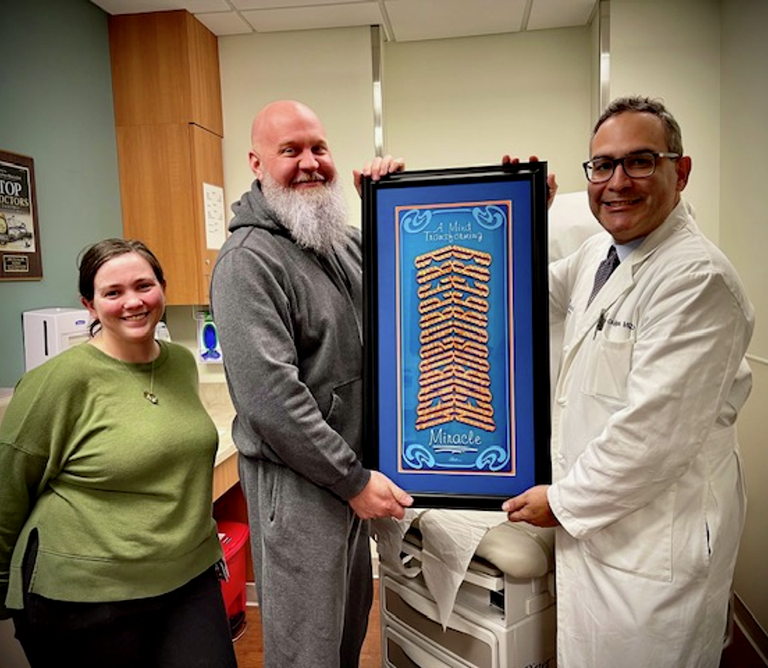 Mike Burton and wife handing Dr. Cajigas a piece of his art