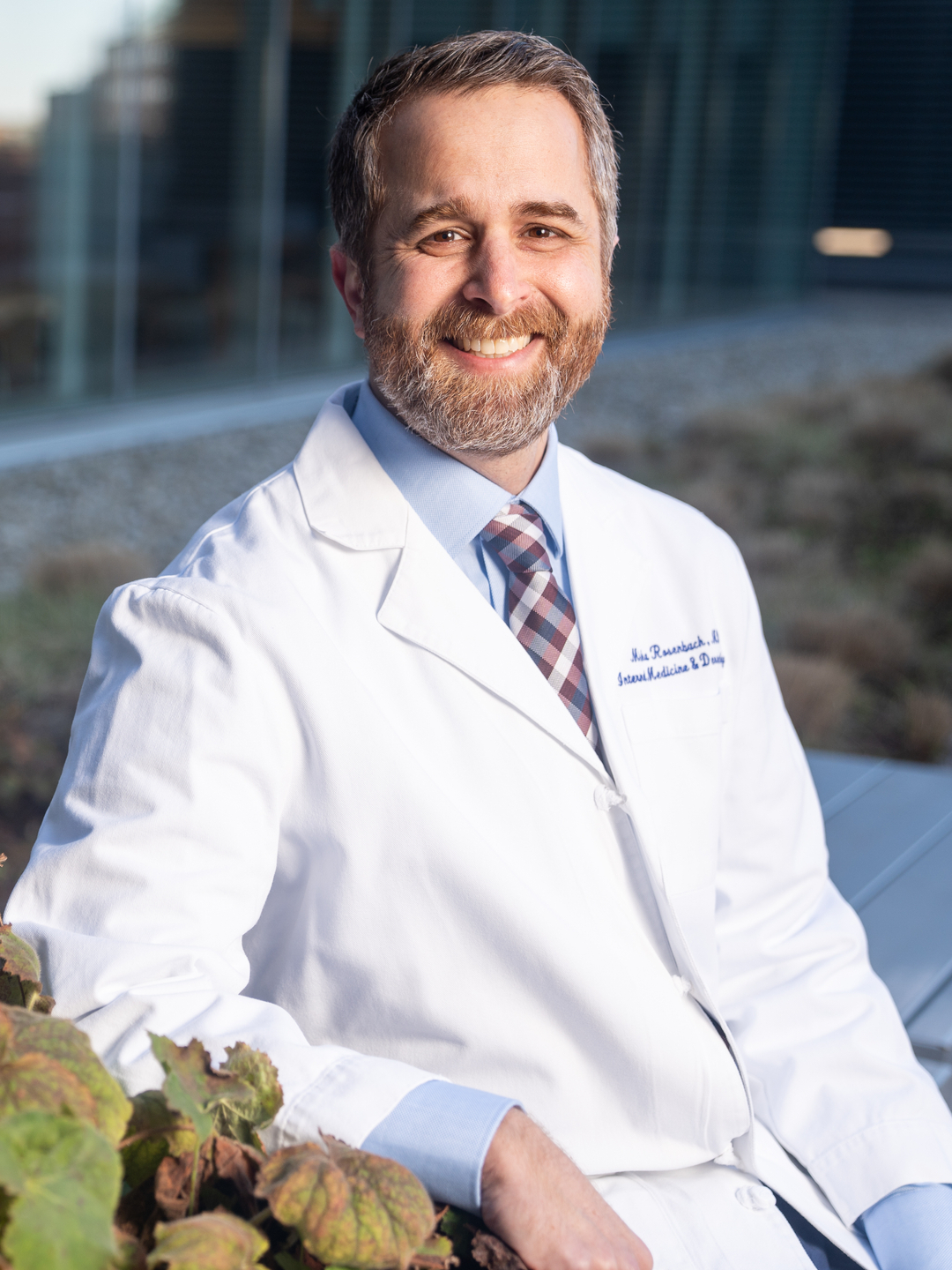 Misha Rosenbach, MD, wearing a white coat and sitting on an outdoor patio