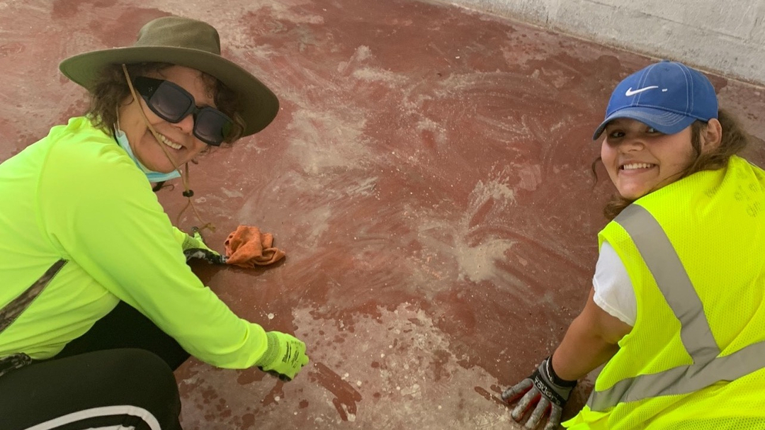 Maria Del Carpio and a teenage girl, both dressed in fluorescent yellow, kneel on a red clay floor and smile