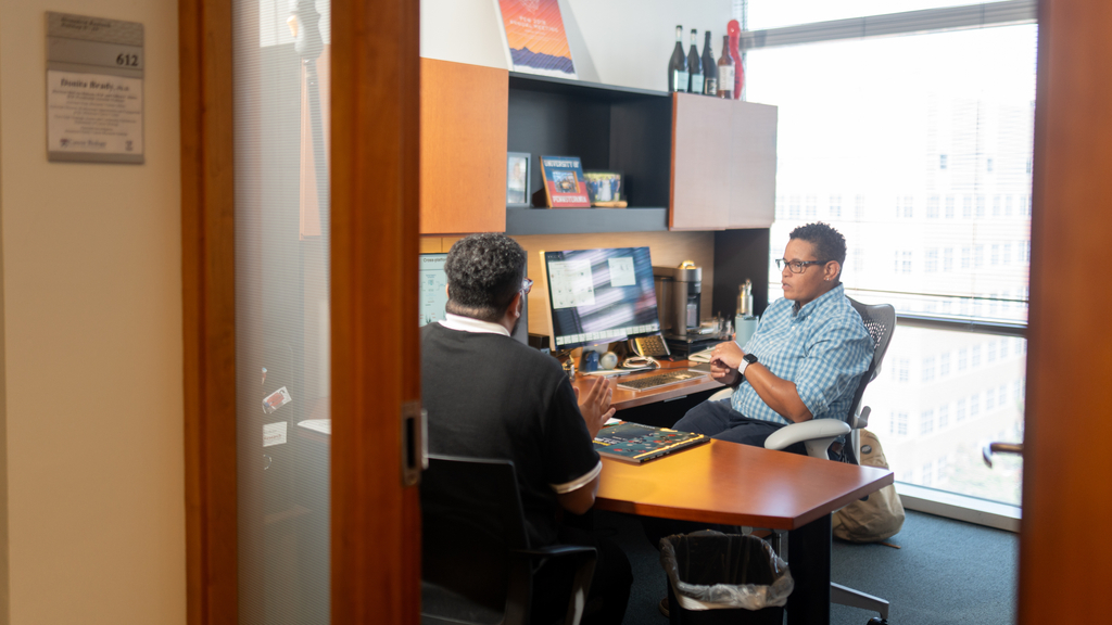 Donita Brady sitting at a desk, speaking with a colleague, in an office.