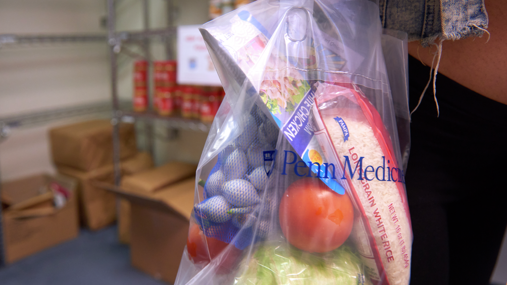 A clear plastic tote bag with the Penn Medicine logo containing food such as a head of cabbage, bag of rice, tomatoes and garlic