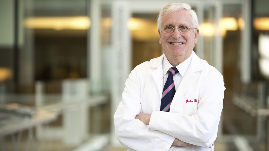John Glick, MD, smiles while standing with his arms crossed, wearing a white coat