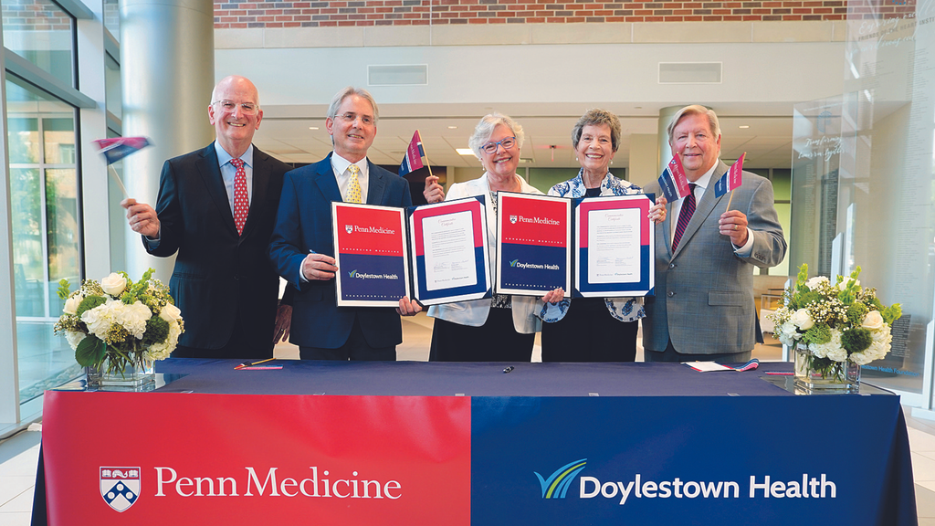 Leaders from Penn Medicine and Doylestown Health wave small flags while holding the signed definitive agreement for the systems' merger.